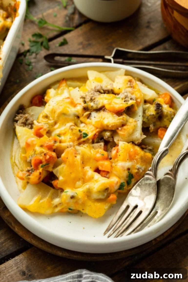 Hearty Cheesy Beef and Potato Bake 7 A perfectly portioned plate of cheesy ground beef and potato casserole is presented with two forks resting beside it, inviting you to dig in.