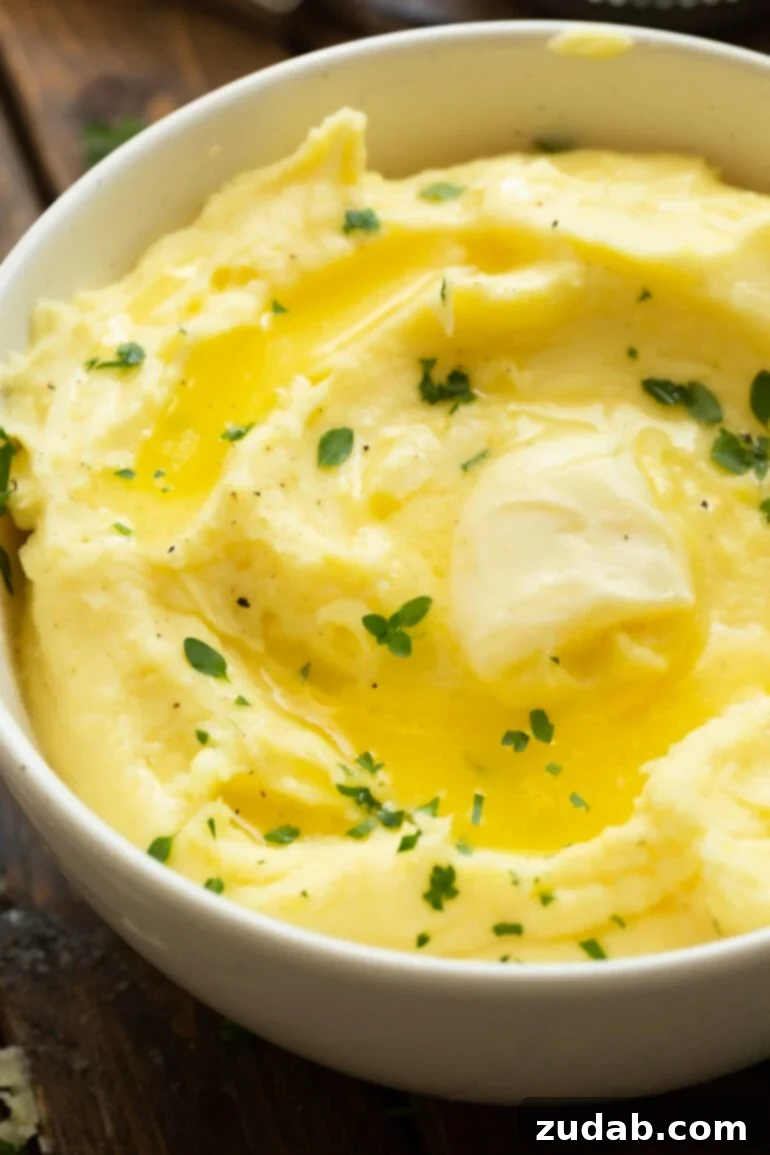 Creamy Instant Pot Mashed Potatoes 2 a photo of a large serving bowl full of creamy mashed potatoes topped with a pat of melting butter and sprinkled with fresh herbs.