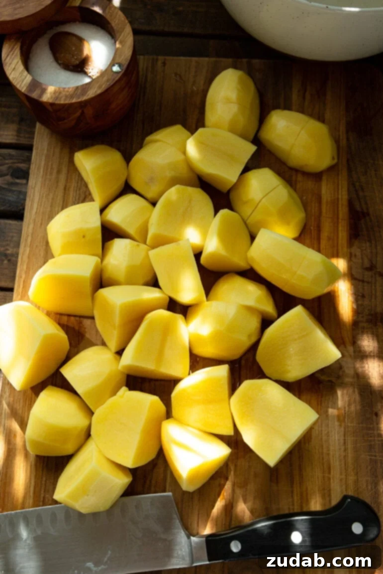 Creamy Instant Pot Mashed Potatoes 4 a photo of several peeled and quartered yukon gold potatoes sitting on a wooden cutting board.