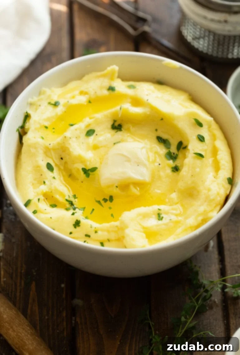 Creamy Instant Pot Mashed Potatoes 8 a photo of a white ceramic bowl full of golden creamy mashed potatoes topped with melting butter and sprinkled with fresh herbs