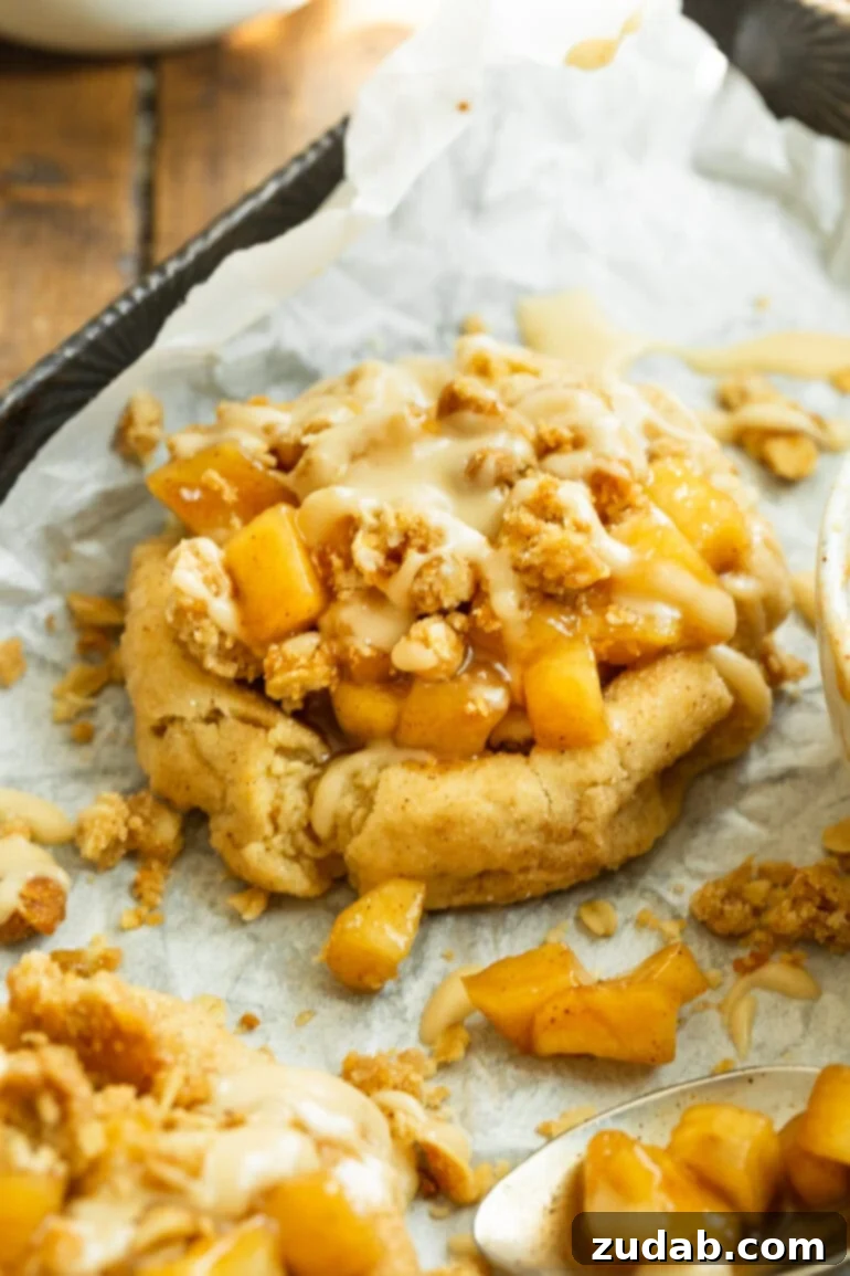A perfectly baked apple crisp cookie with a golden-brown cookie base, a mound of spiced apple filling, crunchy oat streusel, and a delicate vanilla glaze, ready to be enjoyed.