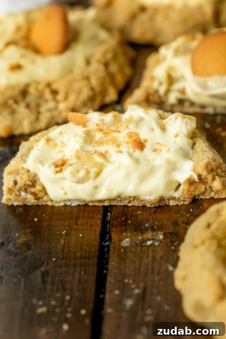 A close-up side view of a banana cream pie cookie, sliced in half to reveal its luscious, creamy cross-section with a visible cookie base and a thick, smooth filling.
