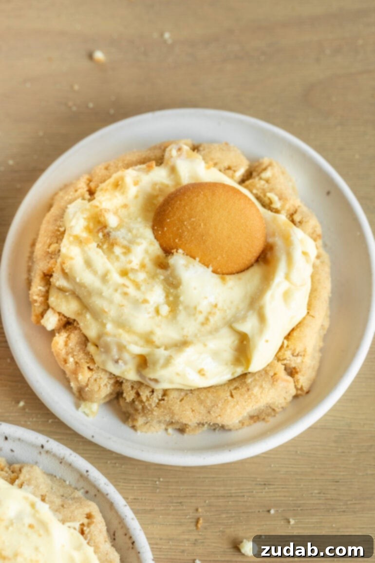 A single, perfectly baked banana cream pie cookie sitting on a small white dessert plate, featuring a golden cookie base topped with creamy banana filling and a Nilla wafer.