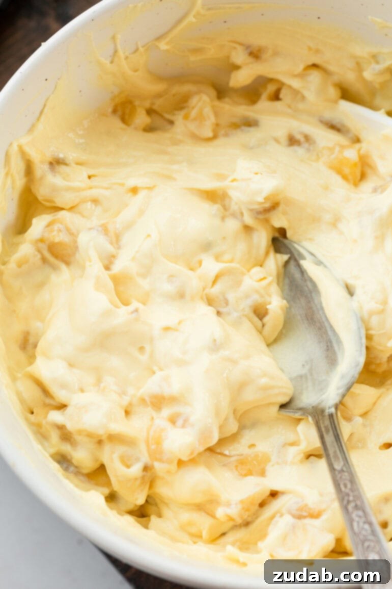 A close-up photo of a large bowl filled with creamy banana pudding, being gently stirred with a spoon, highlighting its smooth texture and visible banana pieces.