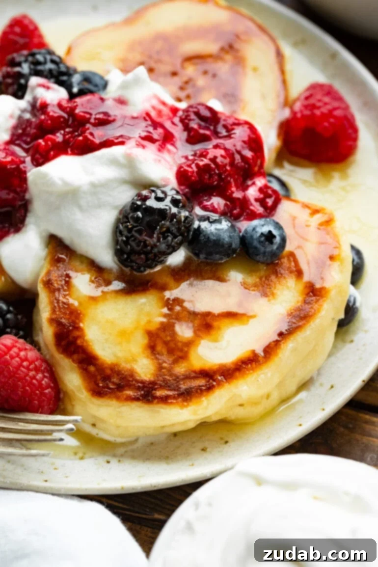 Cloud-Like Fluffy Ukrainian Oladi Pancakes 11 a photo taken close up of a golden crispy oladi pancake topped with syrup and fresh berries.
