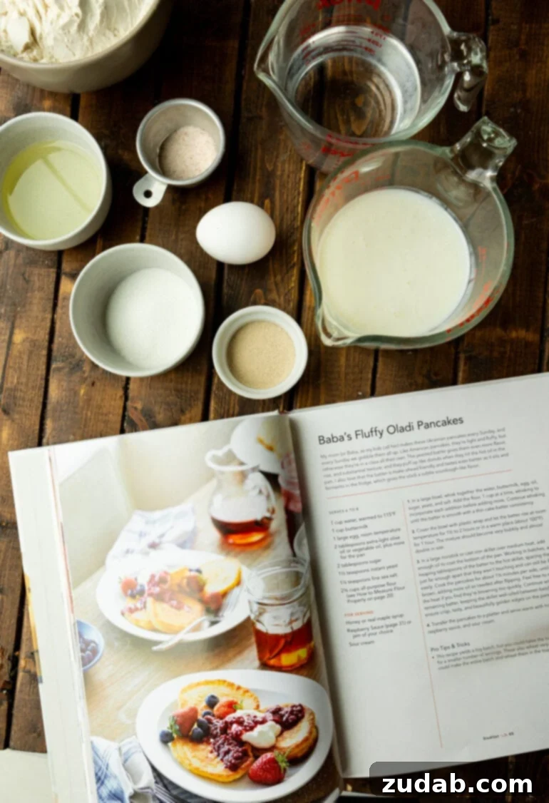 Cloud-Like Fluffy Ukrainian Oladi Pancakes 5 a photo of a cookbook opened to the oladi pancake recipe with all the ingredients for the pancakes sitting around it in separate small bowls and dishes.