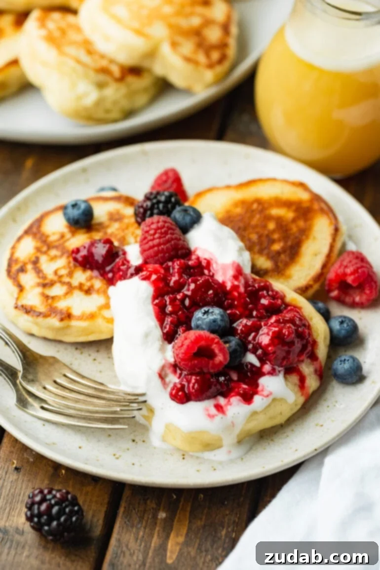 Cloud-Like Fluffy Ukrainian Oladi Pancakes 8 a photo of three crispy golden oladi pancakes sitting on a plate topped with mixed berries and whipped cream.