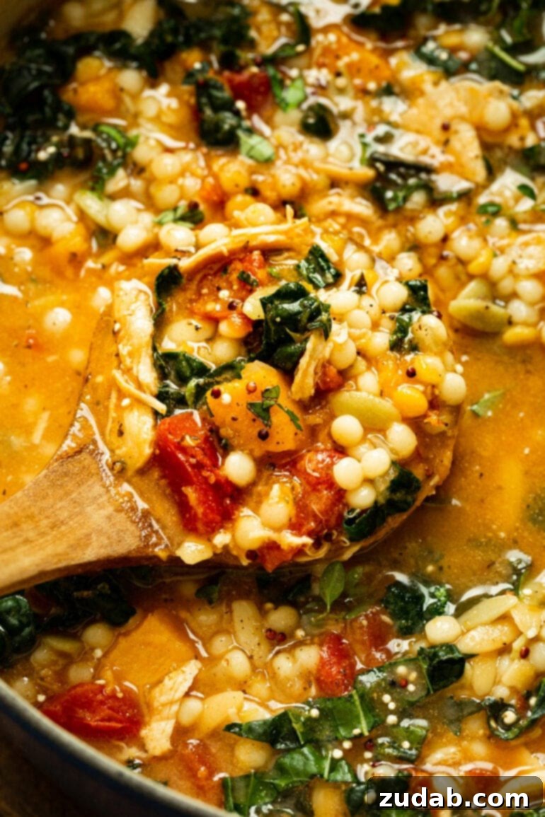 A wooden serving spoon gracefully scooping a generous portion of fall chicken stew, showcasing its rich textures and inviting colors, highlighting the quinoa, butternut squash, and chicken.