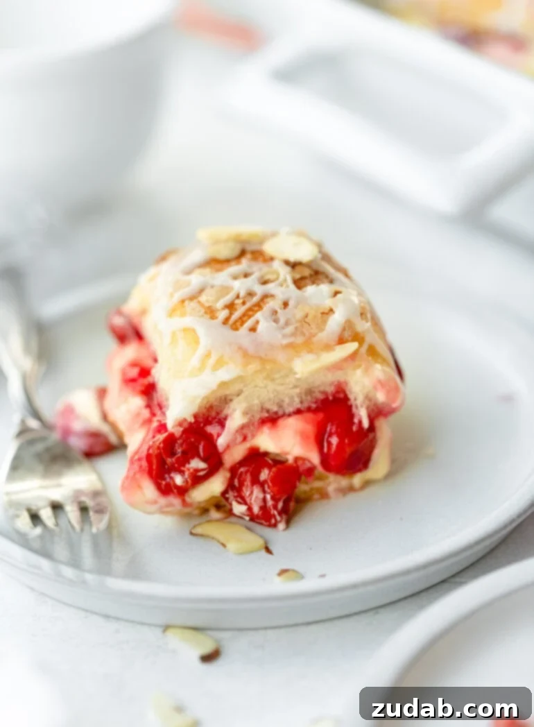 Sweet Cherry Cheese Danish Sliders 2 A perfectly baked cherry cheese danish slider, glistening with sweet glaze and topped with sliced almonds, inviting a bite with a silver fork resting beside it.