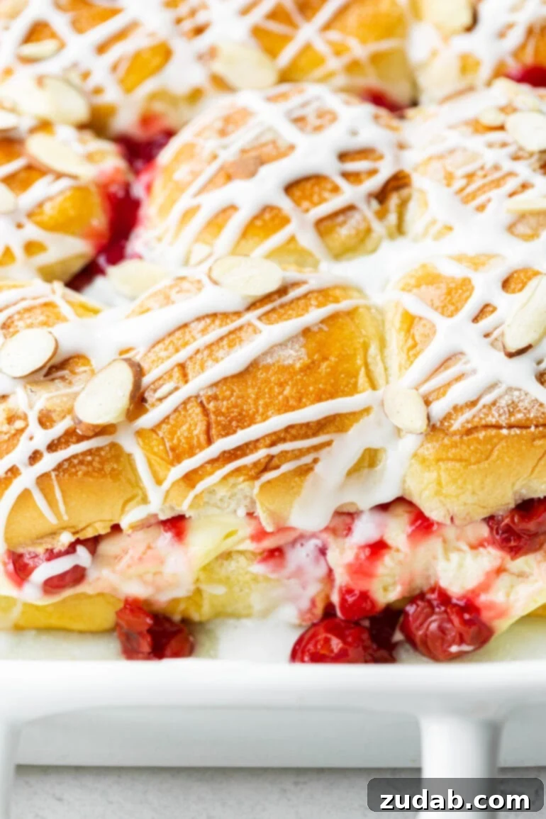 Sweet Cherry Cheese Danish Sliders 3 A close-up shot of a baking dish filled with golden-brown Cherry Cheese Danish Sliders, showcasing the rich cherry pie filling and creamy cheese layers peeking out, beautifully topped with a sweet glaze and sliced almonds.