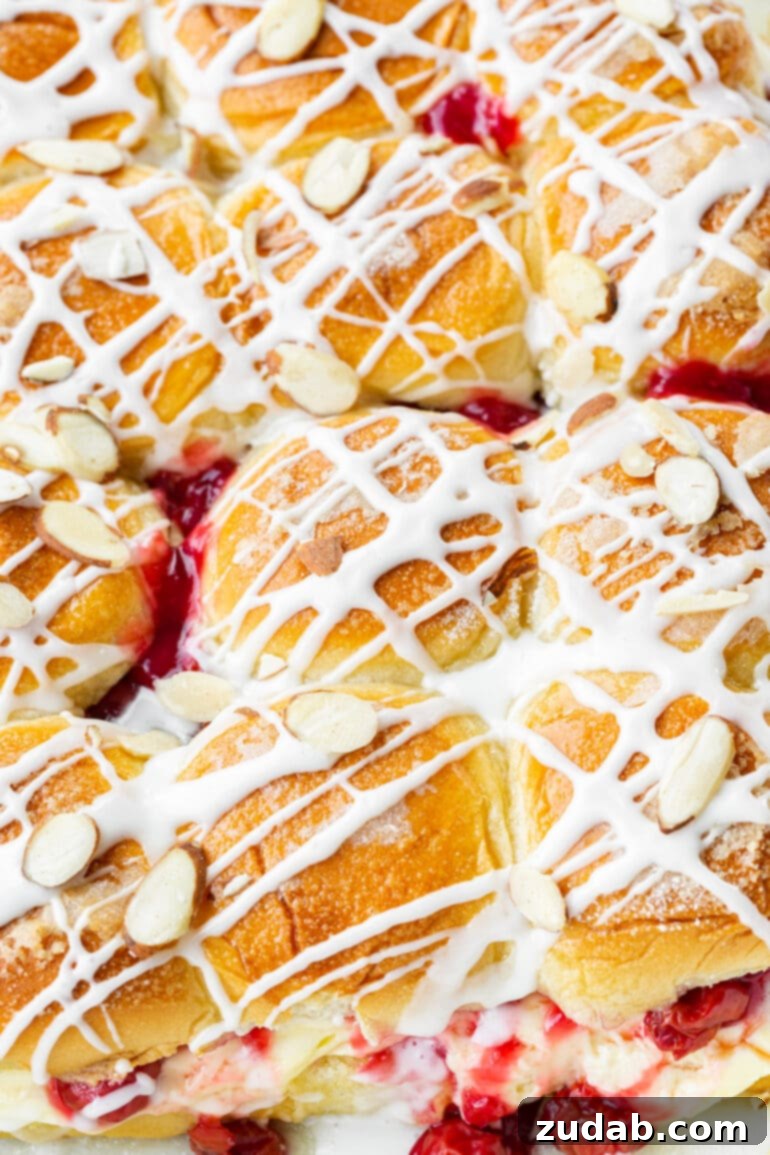 Sweet Cherry Cheese Danish Sliders 6 A baking dish displaying a full dozen of perfectly baked Cherry Cheese Danish Sliders, topped with a creamy white glaze and toasted sliced almonds, ready to be enjoyed at any festive occasion.