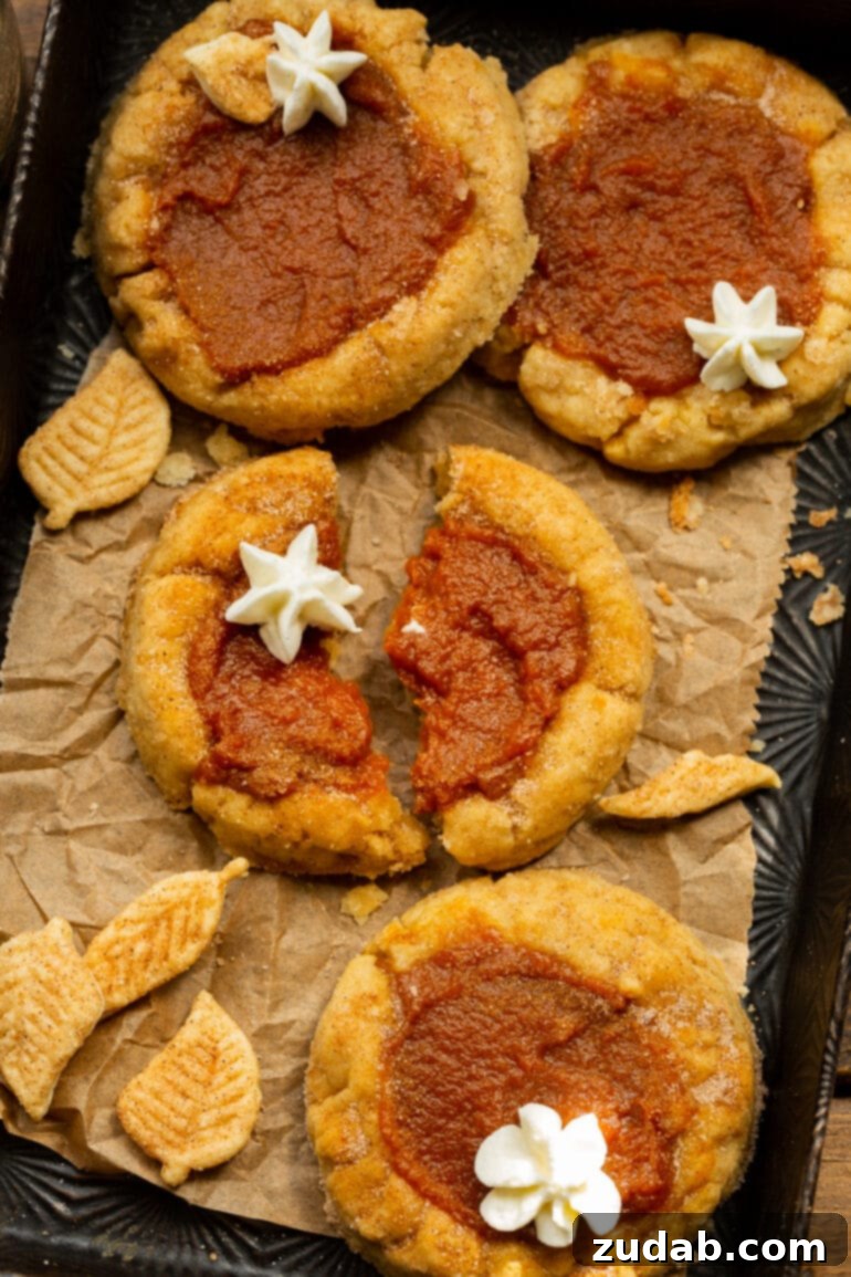 Pillowy Pumpkin Pie Cookies 9 A photo of several pumpkin pie cookies, with the center one broken in half to reveal the creamy filling, topped with a dollop of whipped cream.