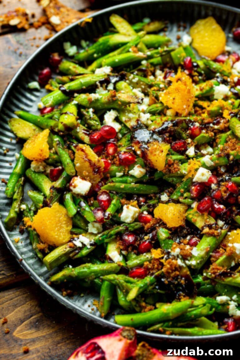 A vibrant asparagus salad mixed with fresh orange segments, glistening pomegranate seeds, and a delicate balsamic glaze drizzle, ready to be served at a holiday gathering.
