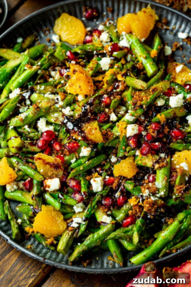 A close-up photo of a vibrant asparagus salad, elegantly arranged with glistening pomegranate seeds, creamy gorgonzola cheese crumbles, bright orange segments, and a rich balsamic glaze, highlighting its bold holiday flavors.