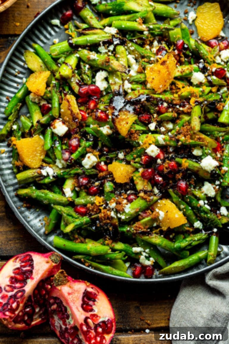 A large serving tray filled with a bright and colorful asparagus, pomegranate, and orange salad, showcasing its fresh and festive appeal.