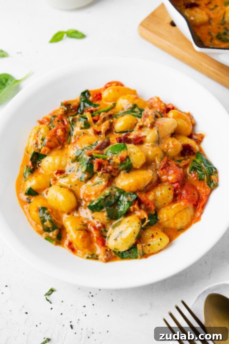 Meals for the Week of November 6-12 7 A vibrant close-up of a white bowl overflowing with soft, pillowy gnocchi tossed in a rich, creamy sauce, featuring bright red sun-dried tomatoes and fresh green spinach leaves.