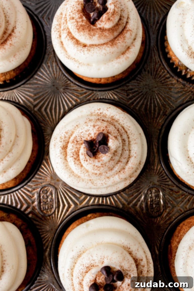 Velvet Pumpkin Chocolate Chip Bliss 12 a photo taken over the top of a decorative muffin tin with baked pumpkin topped with cream cheese frosting