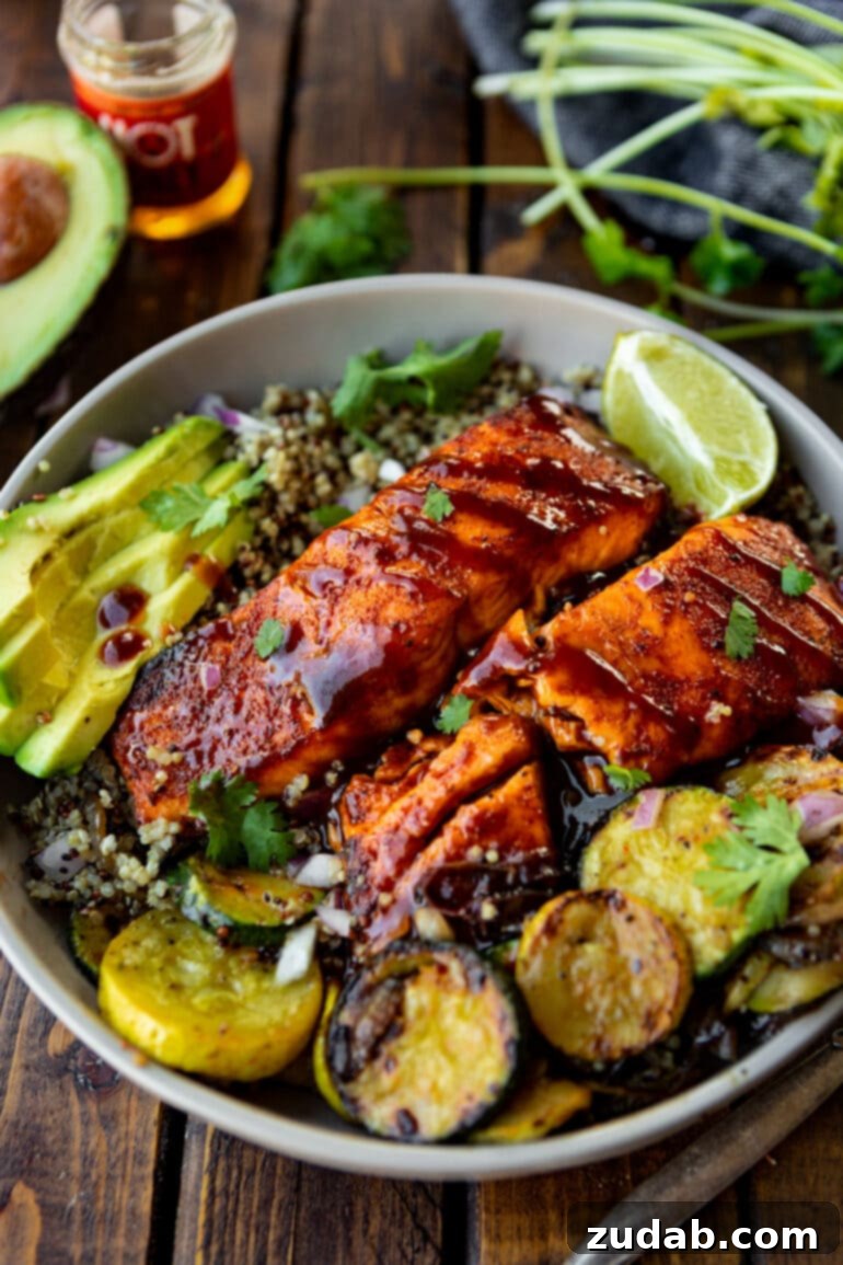 Perfect Air Fryer BBQ Salmon 4 a photo of a two bbq salmon fillets brushed in bbq sauce with a side of grilled squash and sliced avocadoes.