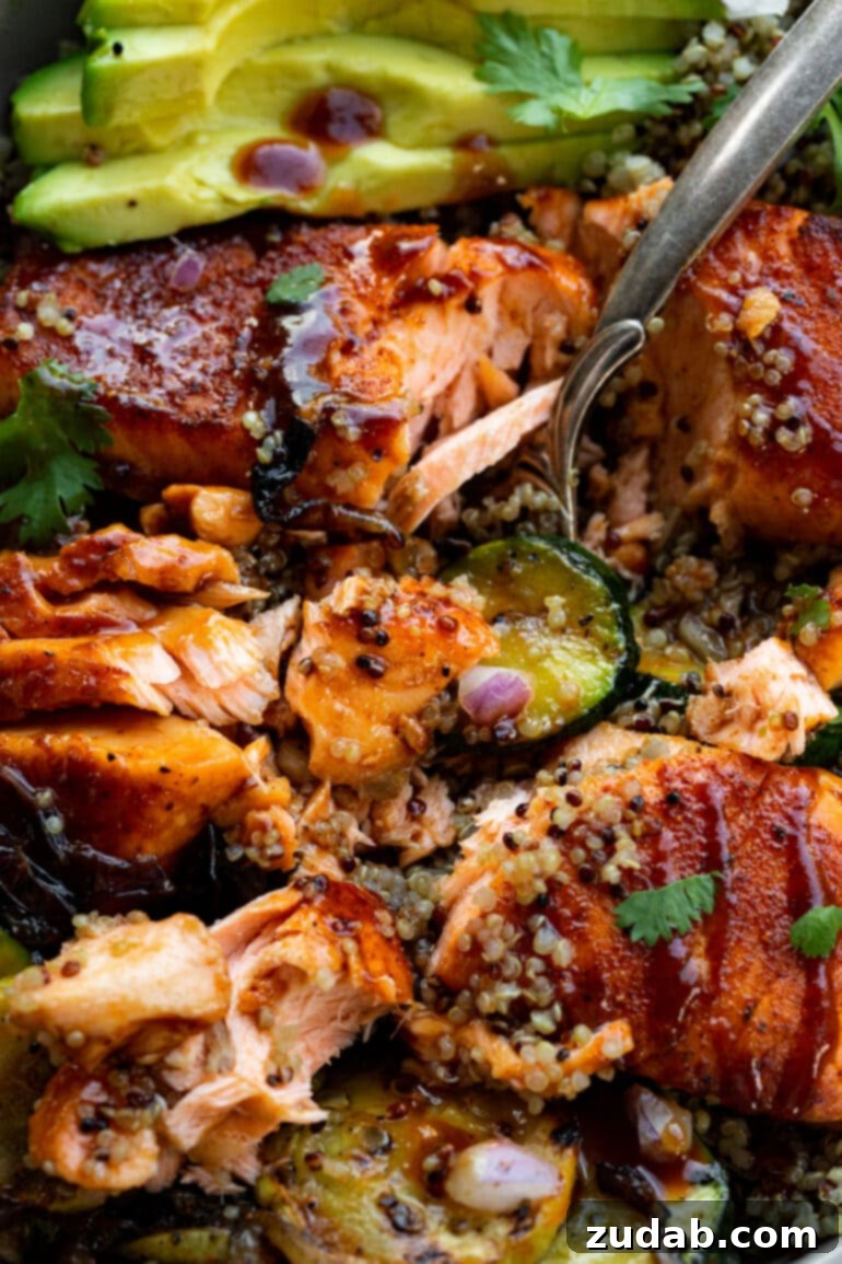 Perfect Air Fryer BBQ Salmon 5 a photo of an air fried bbq salmon fillet that has been flaked apart by a fork on top of a bed of quinoa and grilled zucchini