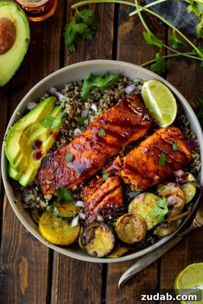 Perfect Air Fryer BBQ Salmon 7 a photo of two air fried salmon fillets brushed with bbq sauce and sitting on a plate next to grilled squash and slice avocados