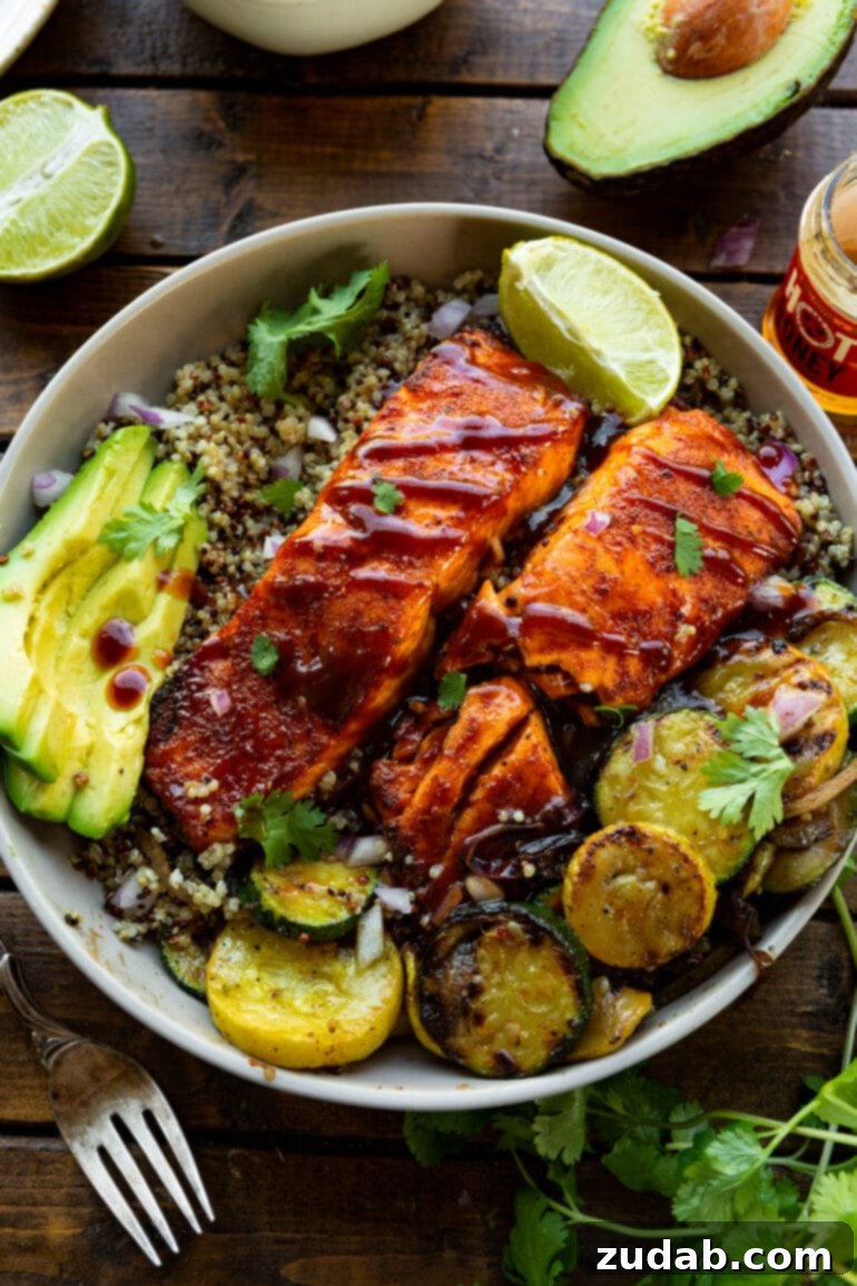 Perfect Air Fryer BBQ Salmon 8 a photo of bbq salmon sitting on a plate on a bed of cooked quinoa with grilled squash sitting next to it, sliced avocados and a lime wedge.