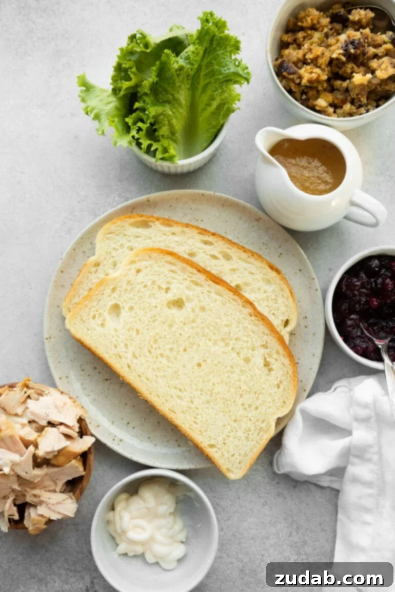 An overhead shot showcasing all the fresh and leftover ingredients laid out on a clean surface, ready to assemble The Gobbler. Ingredients include slices of white bread, vibrant green shredded lettuce, tender leftover turkey, rich turkey gravy, savory stuffing, and glistening cranberry sauce, highlighting the simple yet delicious components of this Thanksgiving leftover sandwich.