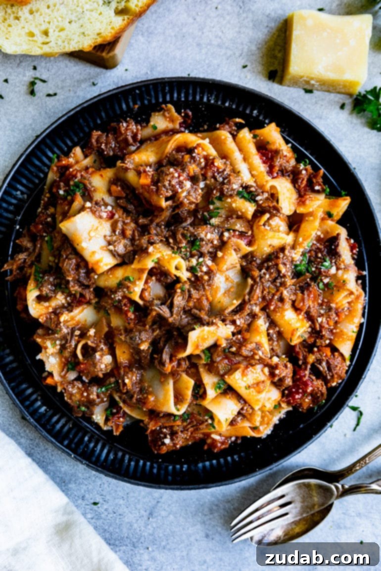 Weekly Menu Plan December 11-17 3 A large black plate piled high with thick, luscious pasta coated in a rich, slow-cooked short rib ragu, garnished with freshly grated Parmesan cheese.