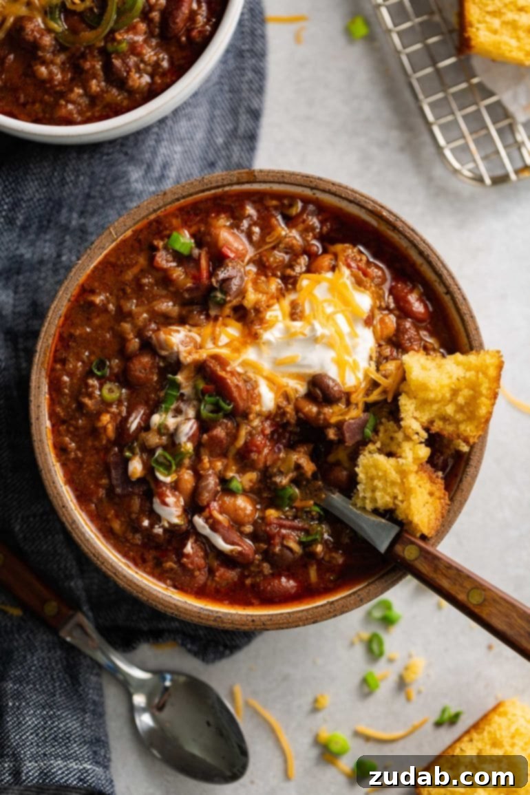 Weekly Menu Plan December 11-17 7 A steaming bowl of rich, hearty chili, brimming with ground beef, beans, and a thick sauce, generously topped with a swirl of sour cream and shredded cheese.