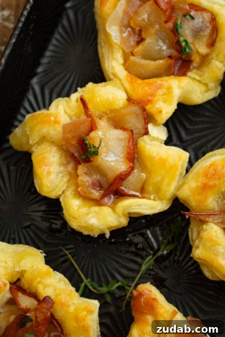 A beautiful display of several golden-baked hot honey pear and brie puff pastry bites, garnished with fresh thyme, ready to be enjoyed.
