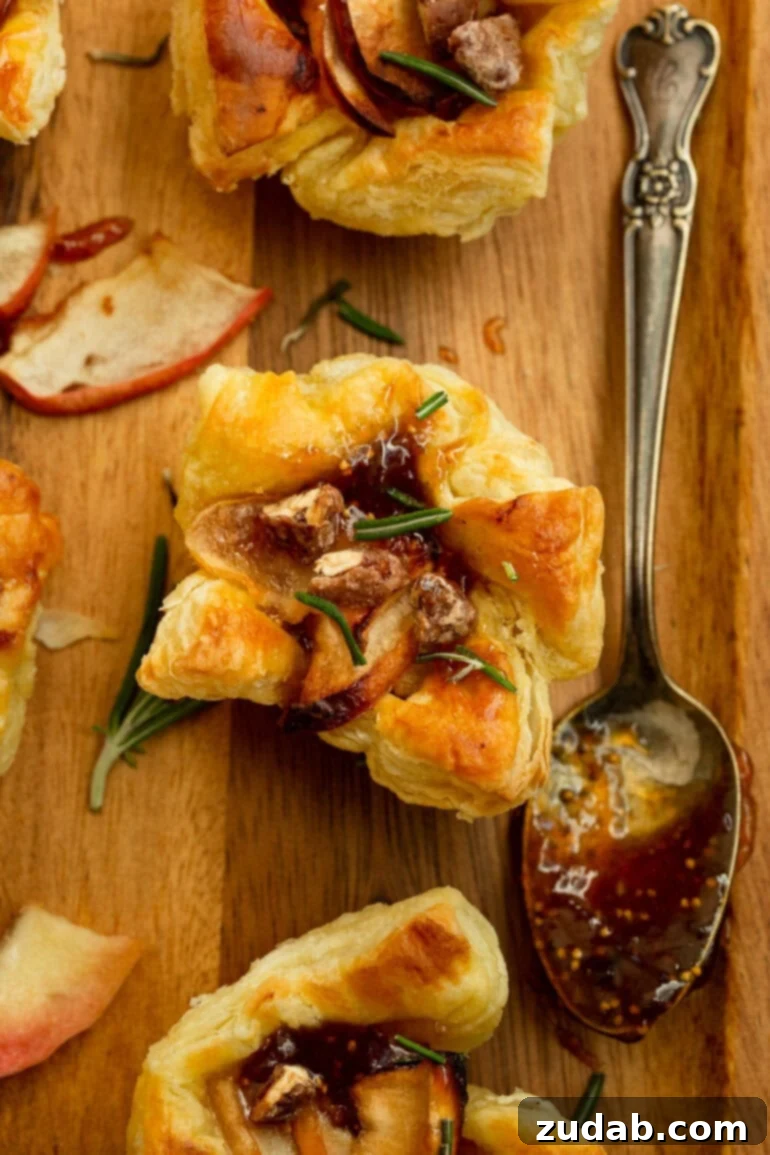 Apple Pecan Brie Bites 2 a photo of golden puff pastry topped with roasted apple slices, gooey brie, and sprinkled with chopped rosemary