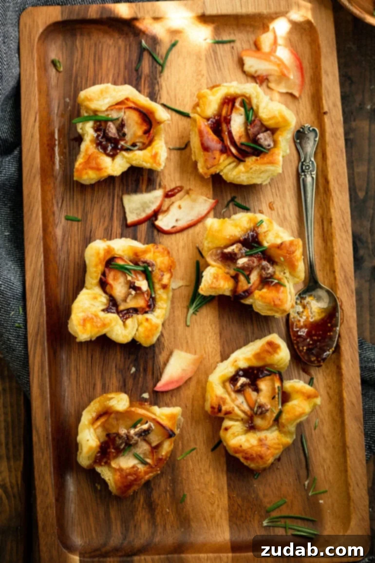 Apple Pecan Brie Bites 4 a photo taken over the top of several golden baked puff pastry bites topped with roasted apples, chopped rosemary and candied pecans