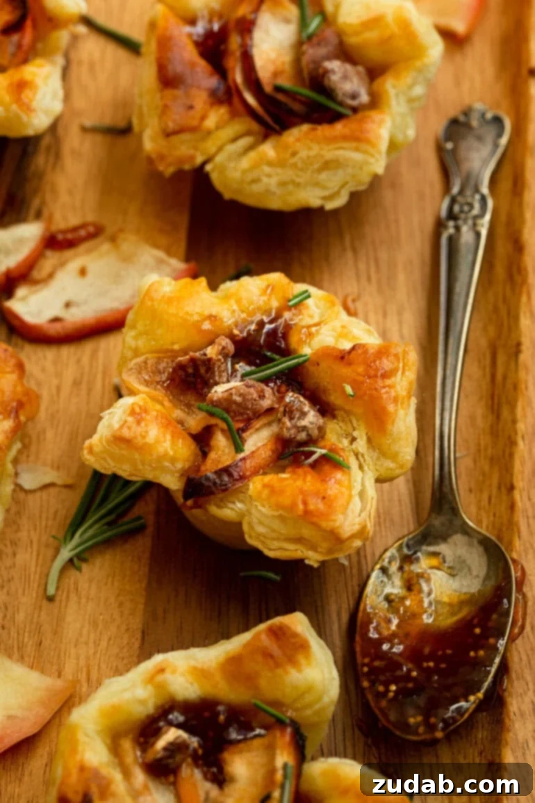 Apple Pecan Brie Bites 5 a photo of a golden baked puff pastry appetizer topped with roasted apples, fresh rosemary, candied pecans with a spoonful of fig jam on the side
