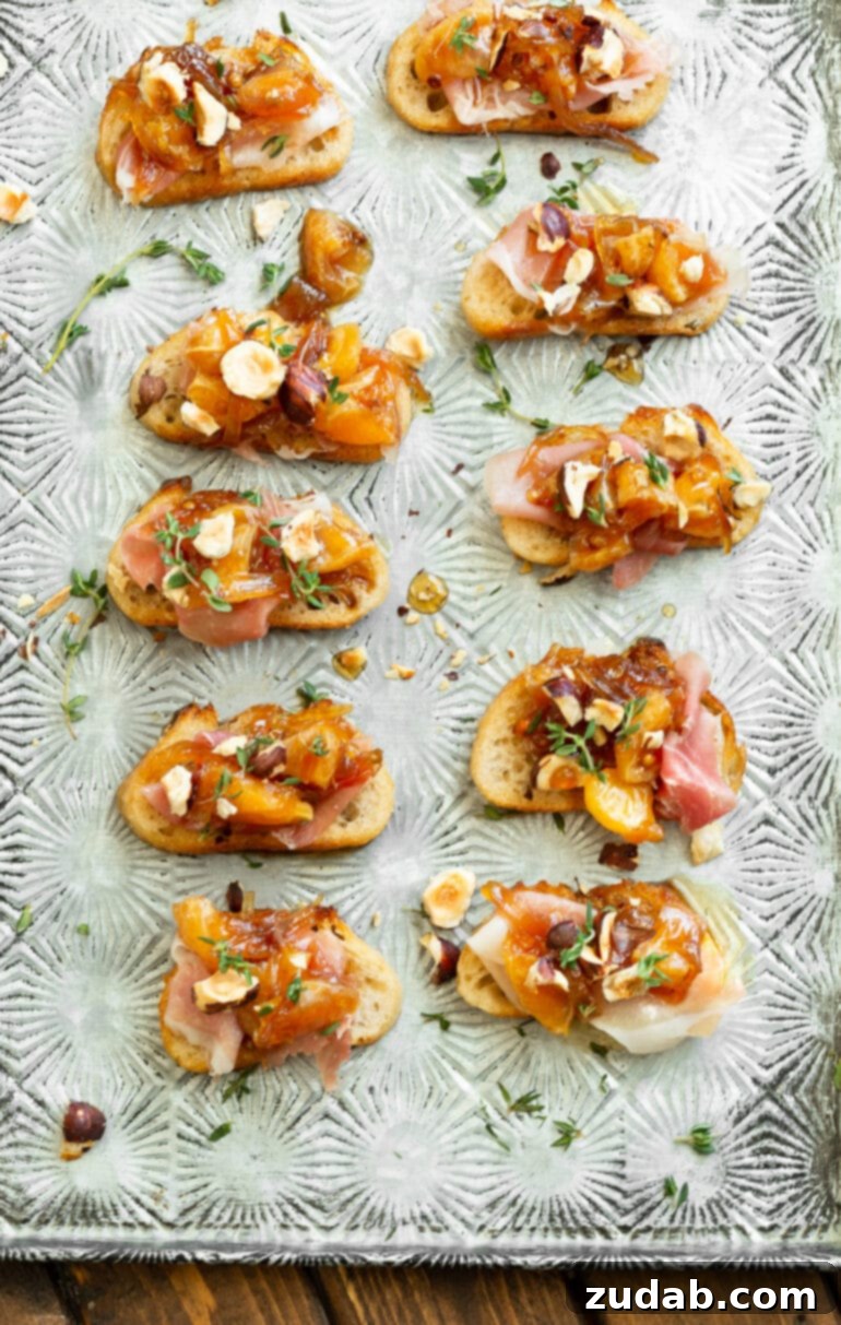 Golden Mandarin Prosciutto Bites 5 Several crostinis arranged on a sheet pan, generously topped with prosciutto, mandarin oranges, toasted hazelnuts, caramelized shallots, and fresh thyme, ready to be served.