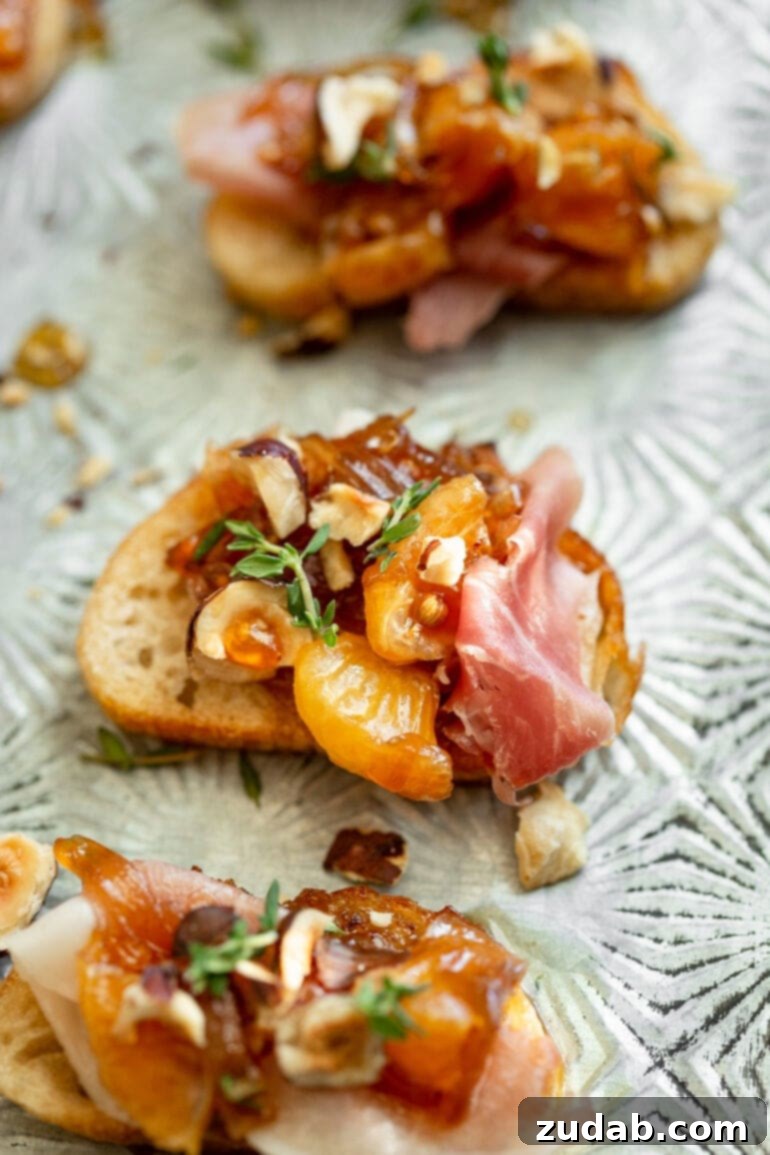 Golden Mandarin Prosciutto Bites 6 A top-down view of three beautifully arranged mandarin orange and prosciutto crostinis, each topped with caramelized shallots, toasted hazelnuts, and fresh thyme, ready to be enjoyed.