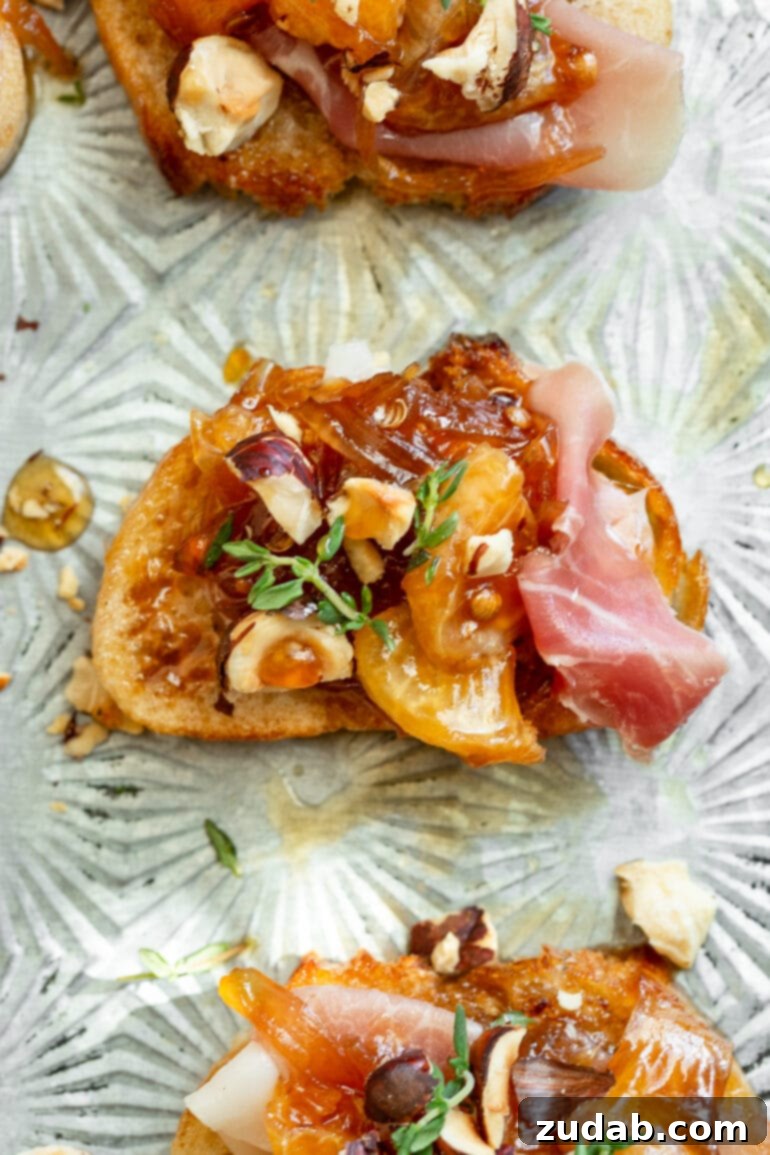 Golden Mandarin Prosciutto Bites 7 A top-down view of a single crostini generously topped with prosciutto, mandarin orange, caramelized shallots, crushed hazelnuts, and fresh thyme, ready for a delectable bite.
