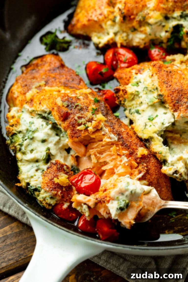 Creamy Spinach Artichoke Stuffed Salmon 5 A fork lifts a mouth-watering bite of creamy spinach artichoke stuffed salmon, surrounded by perfectly roasted cherry tomatoes. The salmon is flaky and the filling is rich.