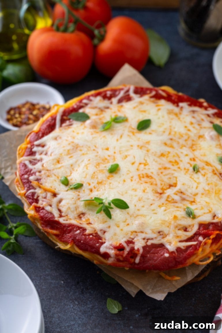 Your Holiday Week Menu December 18-24 7 A hearty Baked Spaghetti Pie nestled in a pie dish, featuring visible layers of spaghetti, a rich red sauce, and bubbling melted cheese, garnished with fresh basil. Complementary ingredients like tomatoes, olive oil, and red pepper flakes are artfully arranged nearby, creating a perfect comfort food scene.