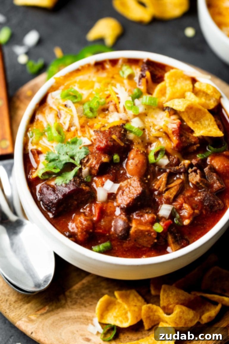 Weekly Meal Plan Dec 25 to 31 7 A close-up of a white bowl brimming with homemade brisket chili, generously topped with Fritos, melting shredded cheese, and vibrant green onions.