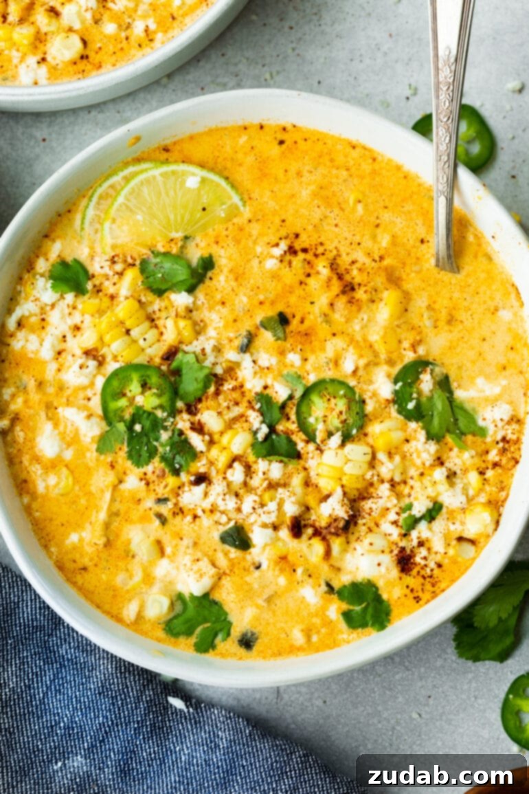 Creamy Elote Chowder 8 A large bowl of golden Elote Corn Soup, richly adorned with bright green cilantro, zesty lime wedges, thin slices of jalapeño, and delicate crumbles of cotija cheese, inviting a warm and flavorful experience.