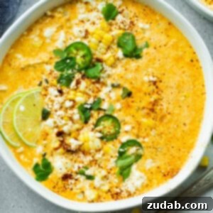 A large bowl of Mexican street corn soup topped with sliced jalapenos, chopped cilantro and lime wedges.
