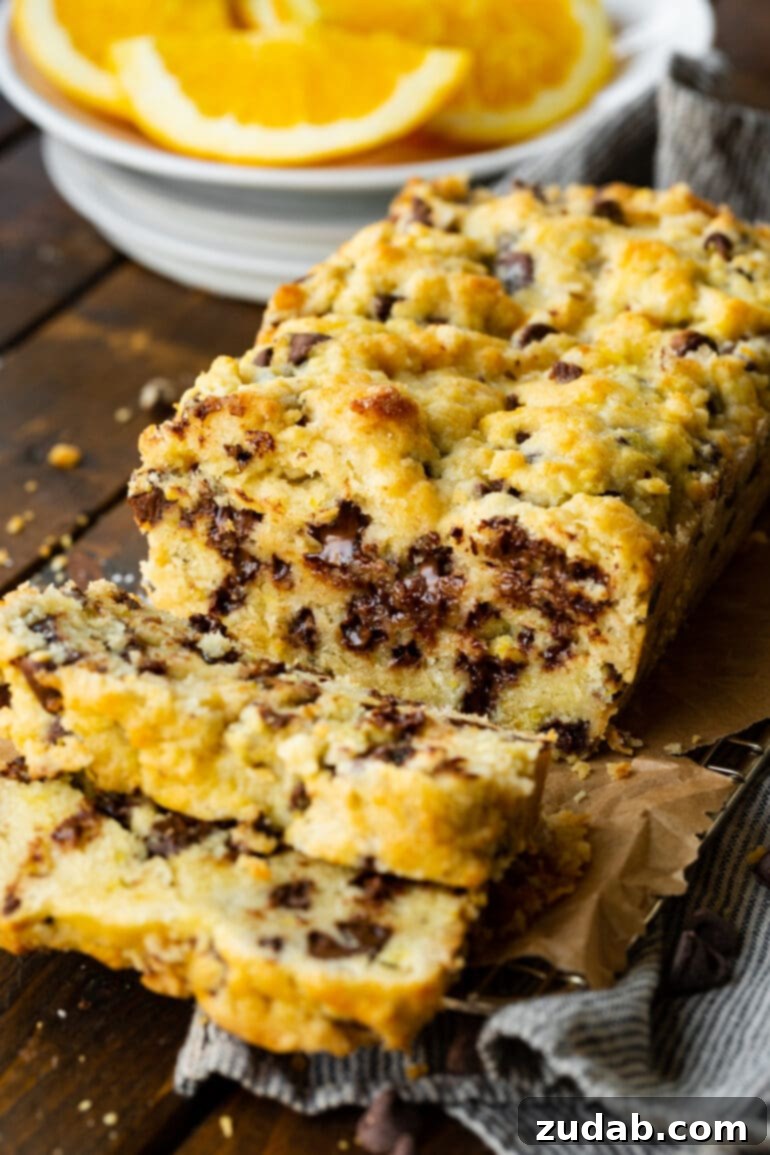 Bright Orange Chocolate Chip Scone Bread 2 A beautifully baked loaf of chocolate orange scone bread, glistening with glaze, with several inviting slices cut off, revealing a generous scattering of chocolate chips within. Perfect for a cozy breakfast or a delightful afternoon snack.