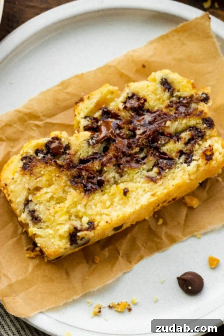 Bright Orange Chocolate Chip Scone Bread 4 A single, delectable slice of orange chocolate scone bread resting on a torn piece of rustic brown parchment paper, highlighting its irresistible texture and the melt of the chocolate chips.