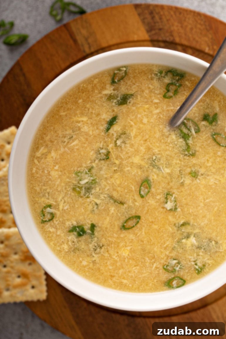 Weekly Meal Plan February 12 to 18 8 A close-up shot of a steaming bowl of homemade Egg Drop Soup, featuring delicate ribbons of egg in a savory clear broth, garnished with fresh green onions and accompanied by crisp saltine crackers in the background, perfect for a light and comforting meal.