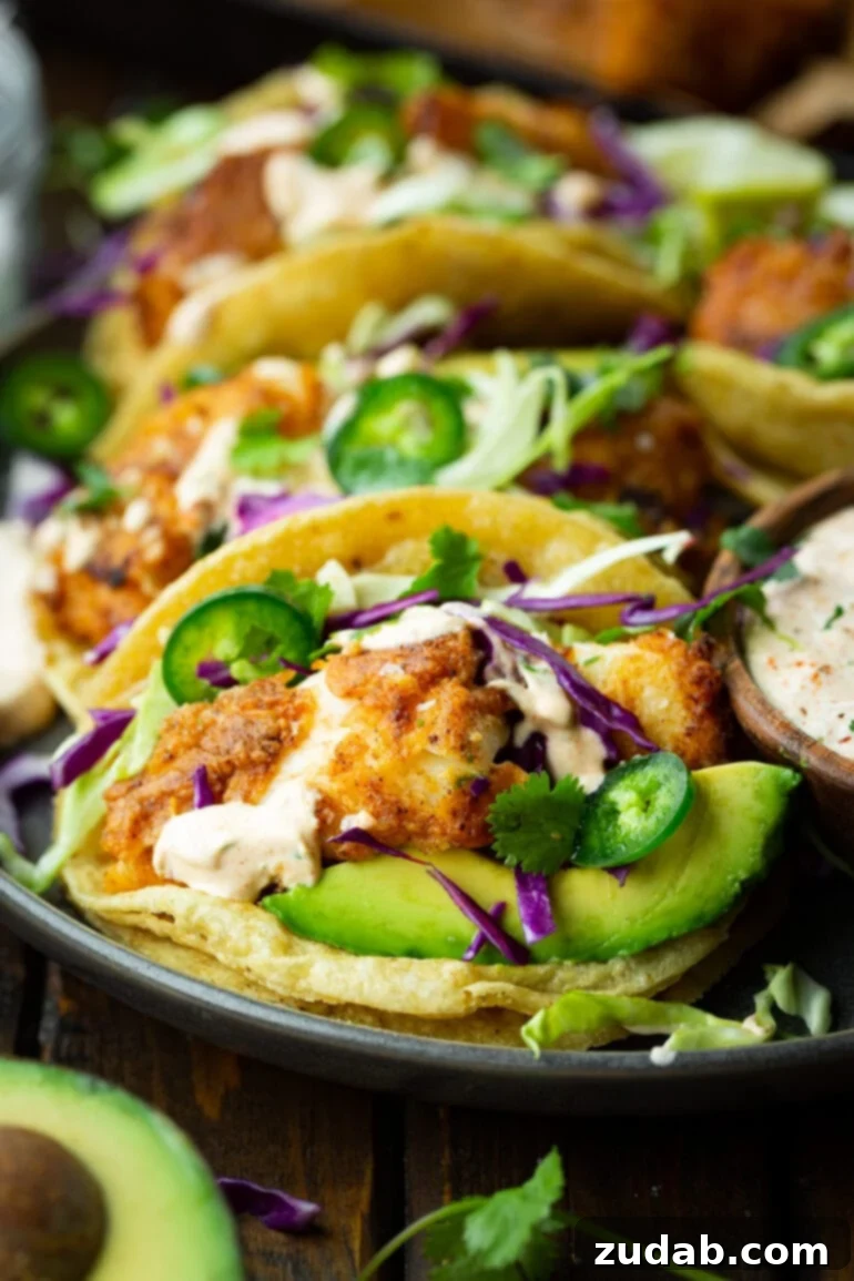 Effortless Homemade Fish Tacos 2 a photo of a tray full of fish tacos with shredded cabbage, sliced jalapenos, sliced avocados and a creamy sauce
