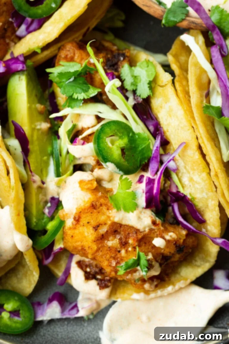 Effortless Homemade Fish Tacos 7 a photo of a fish taco with golden tender fish topped with shredded cabbage, slice jalapenos, chopped cilantro a creamy taco sauce.