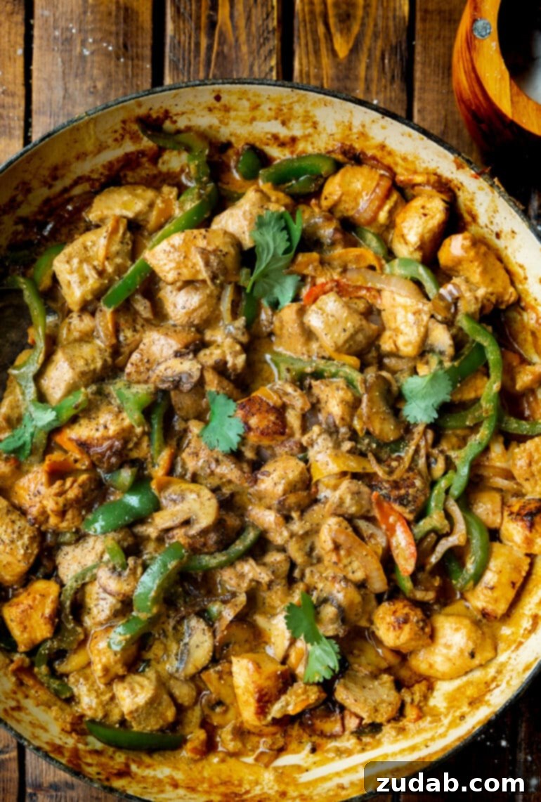 Easy One-Pan Creamy Chicken 2 A photo of a skillet filled with golden chicken chunks, sautéed bell pepper slices, onion slices, and sliced mushrooms, all coated in a rich, creamy sauce, garnished with fresh cilantro.