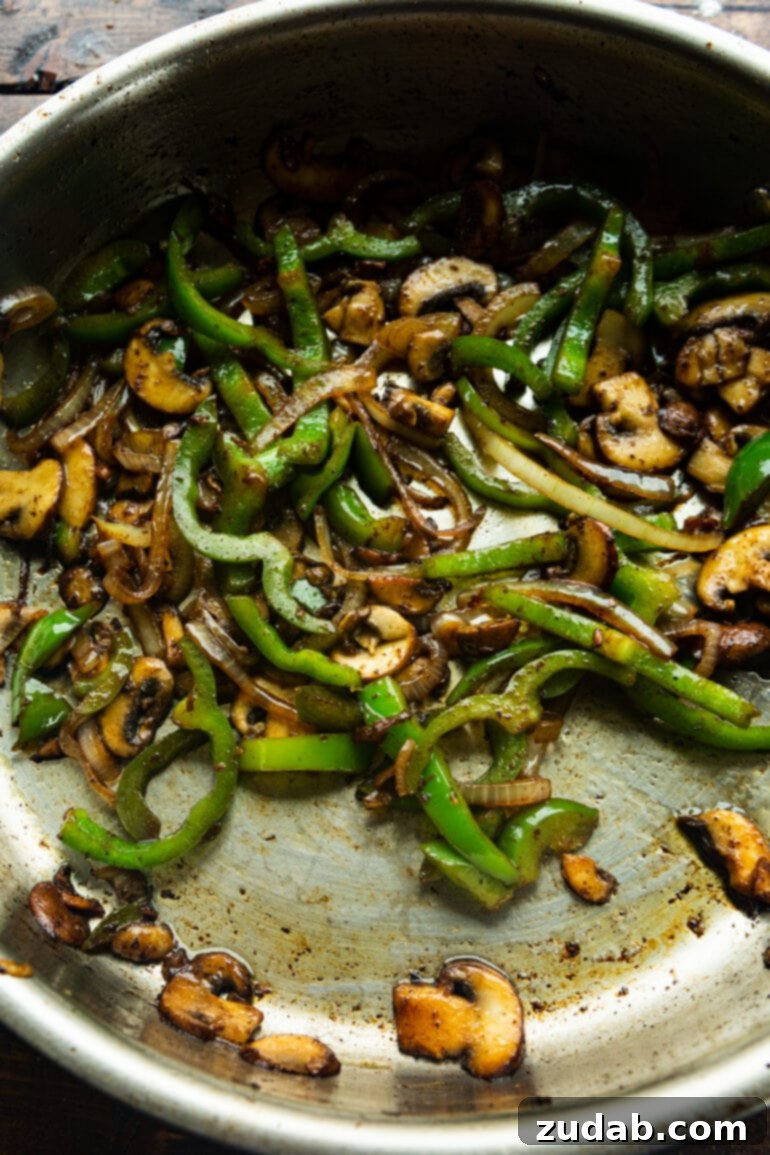 Easy One-Pan Creamy Chicken 5 A vibrant photo of sliced bell peppers and onions being sautéed in a large skillet, with sliced mushrooms about to join them, building layers of flavor for the dish.