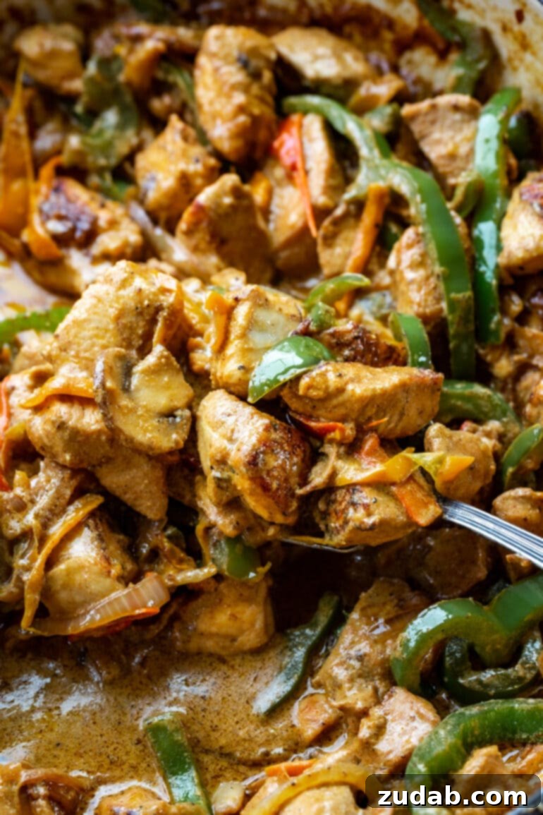 Easy One-Pan Creamy Chicken 6 A silver serving spoon gracefully scooping out a generous portion of creamy Pollo con Crema from a large skillet, ready to be enjoyed.
