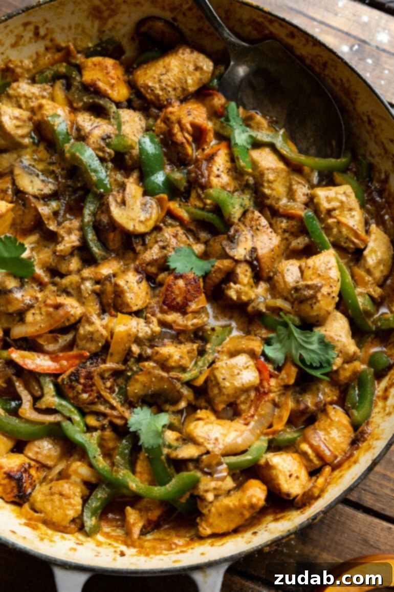 Easy One-Pan Creamy Chicken 9 A vibrant photo of a large skillet filled with golden cooked chicken chunks, sautéed bell peppers, onions, and mushrooms, all generously mixed with a creamy sauce and beautifully topped with fresh chopped cilantro.