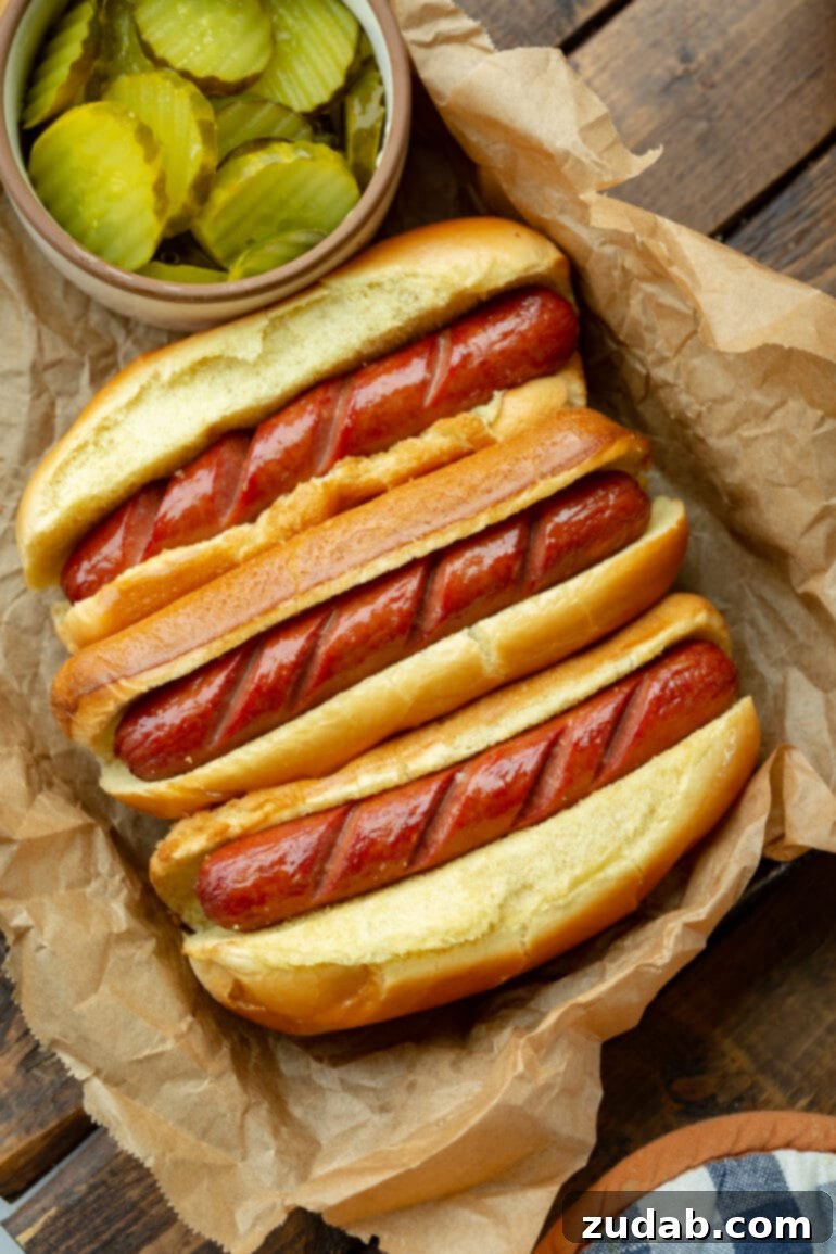 Crispy Air Fryer Hot Dogs 4 An overhead shot of three air-fried hot dogs, scored and nestled in buns, garnished with various vibrant toppings.